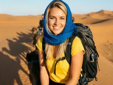 Woman wearing scarf and backpack riding camel in Moroccan desert