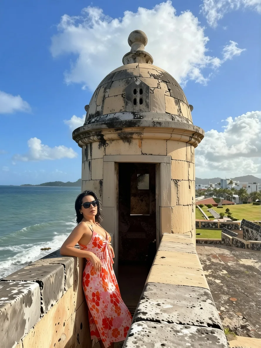 Woman in floral dress posing at historic fort overlooking ocean in Puerto Rico.