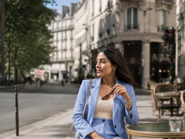 Woman in light blue tailored short suit sitting at outdoor cafe table in Paris