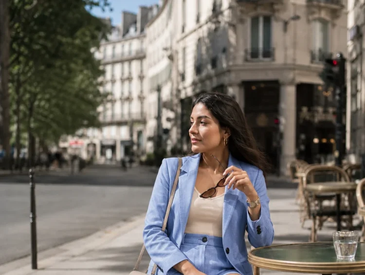 Woman in light blue tailored short suit sitting at outdoor cafe table in Paris