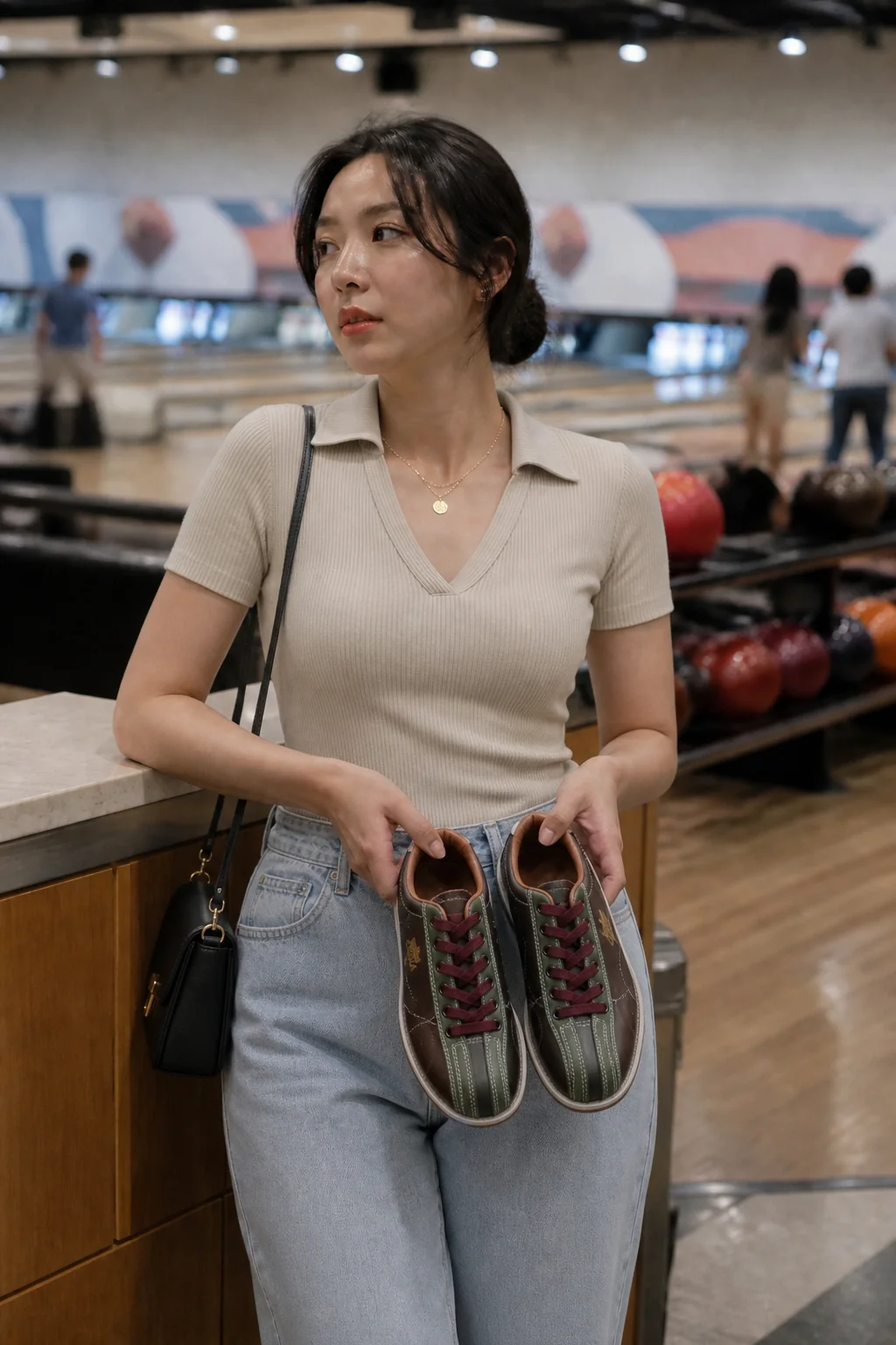 Woman holding bowling shoes at alley counter wearing ribbed polo and jeans.